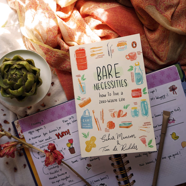 A book. 'Bare Necessities: How to live a zero waste life' placed on a planner around some pens, a stole and a dried flower